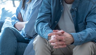 Genç bir erkek ve kadın evdeki koltukta ayrı oturuyorlar, derinden üzgünler, ekonomik zorluklarla boğuşuyorlar, iş güvensizliği, artan faturalar, güven sorunları, aldatma ve yaklaşan bir ayrılık.