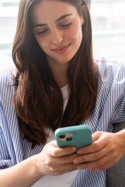 Modern milenyum kadını evinde oturuyor, rahat giyiniyor, akıllı telefon ekranına kayıyor, sosyal medyayı kontrol ediyor, arkadaşlarıyla sohbet ediyor, yeni bağlantılar kuruyor, web sayfaları okuyor.