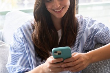 Genç kız rahat bir şekilde evinde kanepede rahat rahat oturuyor, günlük kıyafetlerle gülümsüyor, akıllı telefonu sosyal ağ kurmak, mesajlaşmak, web sayfalarını okumak, çevrimiçi hizmetlere abone olmak ve bilgi araştırmak için kullanıyordu.