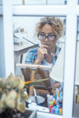 Woman artist painting a colorful and expressive artwork on easel in her home studio, relaxing while using art as a means of expression and creativity, capturing the essence of her emotions through paint. clipart