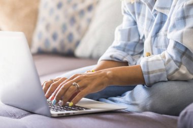 Evden uzakta çalışan bir kadın, dizüstü bilgisayarıyla bir koltukta oturuyor, internette geziniyor, online tarifleri araştırıyor, yeni yemekler okuyor, ve dijital iş aktivitelerine katılıyor.