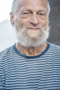 Son sınıf öğrencisi erkek, kırışıklıklarla, mavi gözlerle, beyaz saçlarla ve sakalla neşeli bir şekilde dışarıda huzurlu bir ortamda fiziksel ve zihinsel sağlığa odaklanıyor.