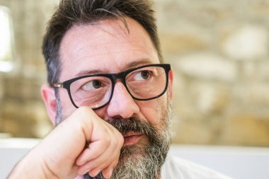 50 yaşında gözlüklü bir adam evde tek başına oturuyor. Yüzü üzüntü ve tefekkürle dolu. Hayatındaki mücadeleleri, yalnızlık hislerini ve duygusal yükleri derinden yansıtıyor.