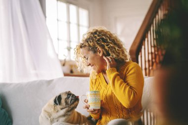 Adult female relaxes on a comfortable sofa at home while engaging with her beloved pug to share genuine comfort and unwavering support, reinforcing daily well-being and emotional balance throughout her steady routine life clipart