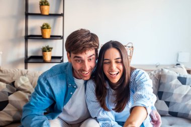 Genç bir çift oturma odasındaki kanepede televizyon izliyor, birlikte rahat bir öğleden sonra geçiriyorlar, kaliteli zaman geçiriyorlar, rahat ve rahat bir ev ortamında uzanıyorlar.