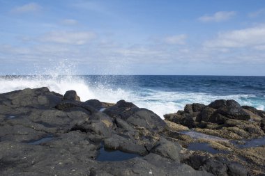 Volkanik kayalarda dalgalar olan okyanus manzarası