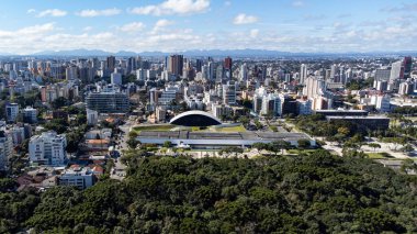 Güneşli bir günde, Curitiba 'daki Oscar Niermeyer Müzesi' ne bakan insansız hava aracı, arka planda şehir ve görüntünün altında Bosque 'tan ağaçlar var..