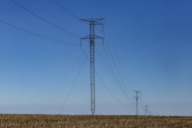 Yüksek voltajlı güç iletim kuleleri. Bulutsuz mavi gökyüzü ve üssü bir tarla..