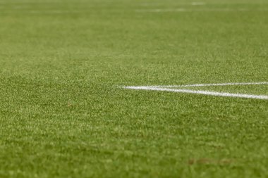 Futbol sahasında sentetik çimenler, altında bir açı, çimlerin yeşili ve bazı beyaz çizgiler var..