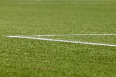 Futbol sahasında sentetik çimenler, altında bir açı, çimlerin yeşili ve bazı beyaz çizgiler var..