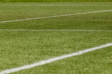 Futbol sahasında sentetik çimenler, altında bir açı, çimlerin yeşili ve bazı beyaz çizgiler var..