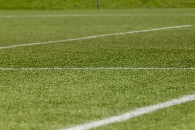 Futbol sahasında sentetik çimenler, altında bir açı, çimlerin yeşili ve bazı beyaz çizgiler var..