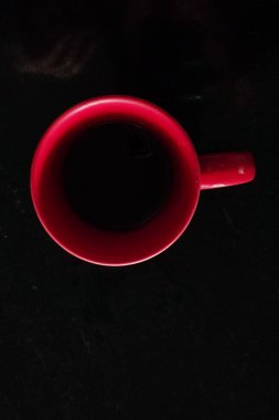 Kahveli kırmızı bir bardak, tanımlanabilecek koyu bir sıvı. İçindekilerin yarısı dolu ve görüntünün arka planı karanlık..