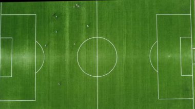 İnsansız hava aracı görüntüsü, zirve açısı, zum hareketi, güneşli bir günde futbol sahasının çok yeşil çimlerle kaplı olması, bazı insanların futbol oynaması..