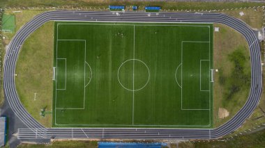 Güneşli bir günde, çimenlerin yeşil renginin göze çarptığı bir futbol sahasının zirvesinden havadan görünüşü.