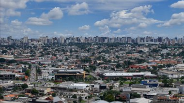 Parana eyaletinin başkenti Curitiba 'nın panoramik görüntüsü. Arka planda binaları ve mavi gökyüzünü bulutlar arasında görebilirsiniz, ve ön planda çeşitli binaları ve caddeleri görebilirsiniz..