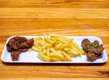 Kızarmış tavuk kanadı, patates ve patates kızartması. Tahta masadaki beyaz tabakta.