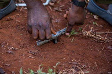 Üniformalı Afrikalı bir adam yerde bir bıçak tutuyor.