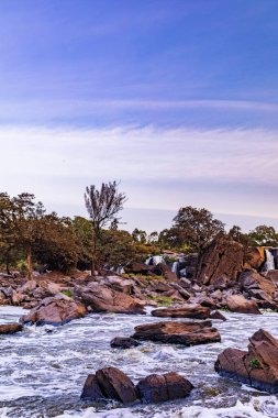 Mavi gökyüzünün altında yeşilliklerle çevrili güzel bir kaya görüntüsü.