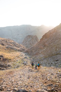 Dağlarda sırt çantalı üç turist. Turistler kayalık dağlarda seyahat ederler. Dağ yürüyüşünde aktif dinlenme. Dağlarda macera. Grup yürüyüşleri