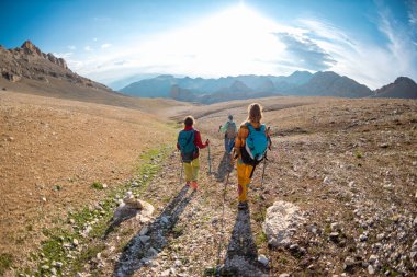 Dağlarda sırt çantalı üç turist. Turistler kayalık dağlarda seyahat ederler. Dağ yürüyüşünde aktif dinlenme. Dağlarda macera. Grup yürüyüşleri