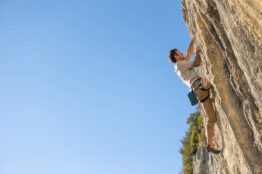 Güçlü bir adam yüksek irtifada bir kayaya tırmanır, kayalıklarda bir dağcı treni, eğitim gücü ve dayanıklılık.