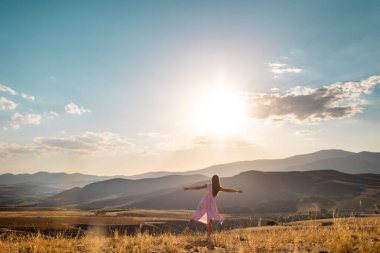 a girl in a pink dress walks across the field against the backdrop of mountains. the concept of freedom and joy.