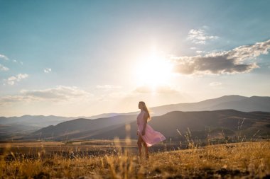 a girl in a pink dress walks across the field against the backdrop of mountains. the concept of freedom and joy.