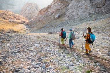 Dağlarda sırt çantalı üç turist. Turistler kayalık dağlarda seyahat ederler. Dağ yürüyüşünde aktif dinlenme. Dağlarda macera. Grup yürüyüşleri