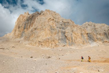Dağlarda yürüyüş yapan iki kız. Sırt çantalı genç kızlar gökyüzüne karşı bir dağ yolunda yürüyorlar..