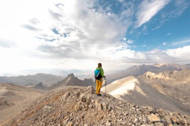 A girl with a backpack stands on top of a mountain. hiking in the mountains. Girl with a backpack in the mountains