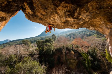 Kız kaya tırmanışçısı bir ormanın arka planına ve mavi dağlara tırmanır. Dağcı ekipman kullanarak zor bir yoldan geçiyor. Türkiye 'de kaya tırmanışı.