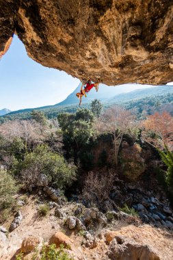 Kız kaya tırmanışçısı bir ormanın arka planına ve mavi dağlara tırmanır. Kaya tırmanışçısı zor bir yolda dinleniyor. Türkiye 'de kaya tırmanışı.