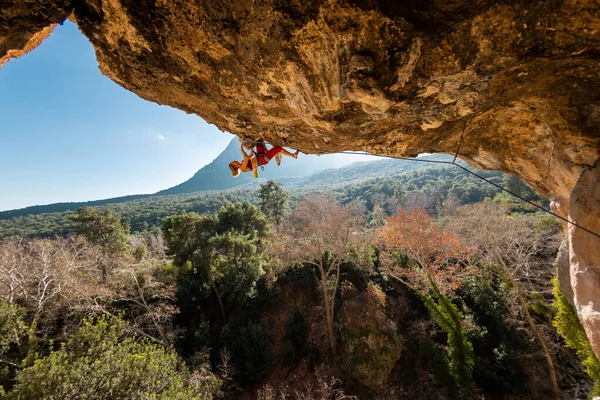 Kız kaya tırmanışçısı bir ormanın arka planına ve mavi dağlara tırmanır. Dağcı ekipman kullanarak zor bir yoldan geçiyor. Türkiye 'de kaya tırmanışı.