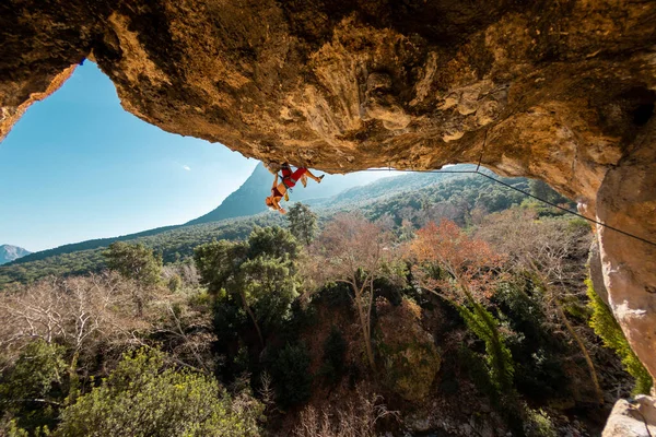 A young rock climber on an overhanging cliff. The climber climbs the rock. The girl is engaged in sports climbing. Sports in nature.