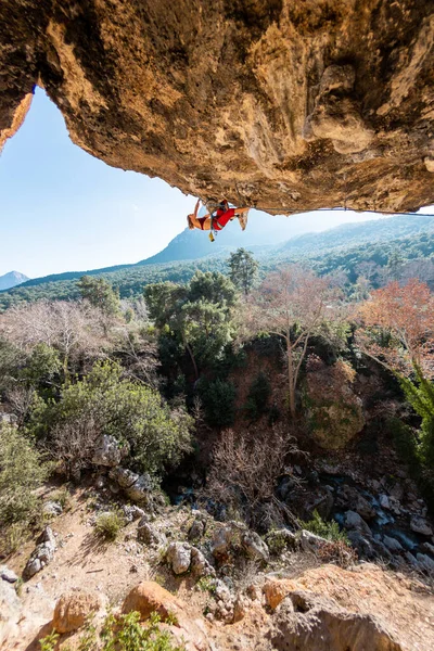 A young rock climber on an overhanging cliff. The climber climbs the rock. The girl is engaged in sports climbing. Sports in nature.