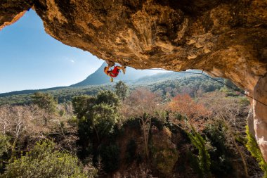 Kız kaya tırmanışçısı bir ormanın arka planına ve mavi dağlara tırmanır. Dağcı ekipman kullanarak zor bir yoldan geçiyor. Türkiye 'de kaya tırmanışı.