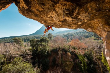 girl rock climber climbs a rock against the backdrop of a forest and blue mountains. rock climber resting on a difficult route.