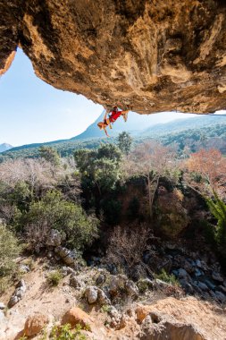 Kız kaya tırmanışçısı bir ormanın arka planına ve mavi dağlara tırmanır. Kaya tırmanışçısı zor bir yolda dinleniyor. Türkiye 'de kaya tırmanışı.
