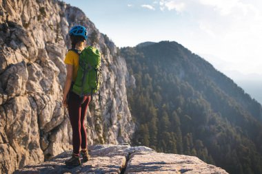 Sırt çantası ve kasklı kadın tırmanışçı yaz günü tırmanmadan önce muhteşem dağ manzarasının tadını çıkarıyor. macera ve dağcılık kavramı. 