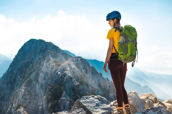 Woman climber with backpack and helmet enjoys amazing mountain view before climbing on a summer day. adventure and mountaineering concept.