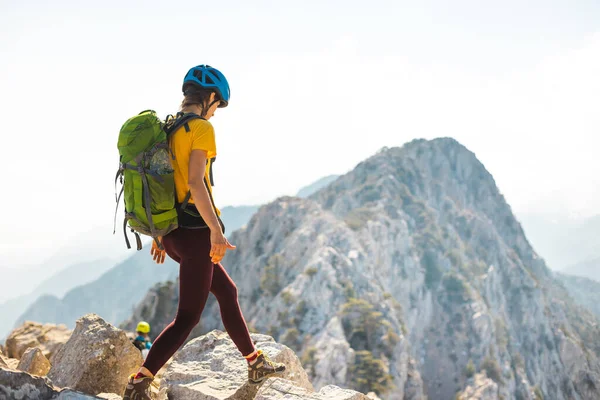 女性のバックパックと山の中でヘルメットを登る リュックを持った女の子が山脈を歩いている 冒険と登山の概念 山の中でバックパックを持ってハイキングをし — ストック写真