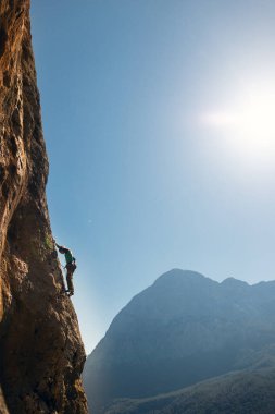Kız gökyüzü ve dağların arka planında kayalara tırmanıyor. Sporcu kız kaya tırmanışı yapıyor. ekstrem spor
