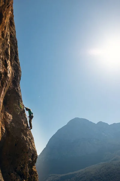 The girl climbs the rocks against the background of the sky and mountains. sports girl is engaged in rock climbing. extreme sport