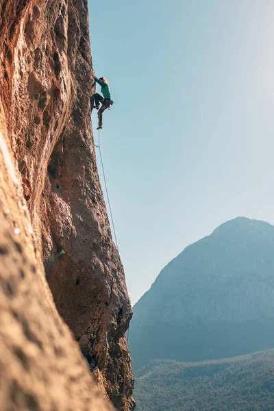 The girl climbs the rocks against the background of the sky and mountains. sports girl is engaged in rock climbing. extreme sport
