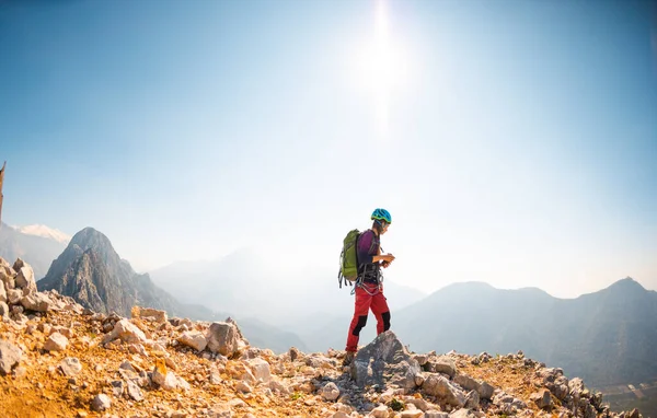 戴着头盔和背包的女登山者站在山脉上 背景是群山和天空 登山及远足 — 图库照片