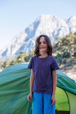 Neşeli çocuk bir çadır ve bir dağın arkasında duruyor. Çocuklarla seyahat etmek. Aile tatili ve seyahat.