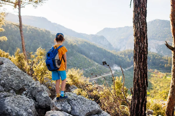 旅行中の子供 バックパックを持った観光客が山道に立って山を眺めます ハイキングや健康的なライフスタイルです 子供たちとの冒険の休日 — ストック写真