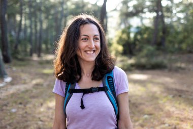 Sırt çantalı genç bir kız ormanda seyahat ediyor. Ormanda ve dağlarda turist yürüyüşü. Kız kameraya gülümsüyor. yürüyüş ve macera konsepti.