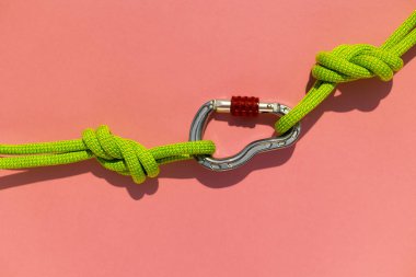 İple çizilmiş karabina renkli bir arka planda yatıyor. Tırmanma ve dağcılık ekipmanları. Güvenilir bağlantı. Güvenlik halatı. Sekiz nod. Güvenilirlik ve güç kavramı. Boşluğu kopyala.